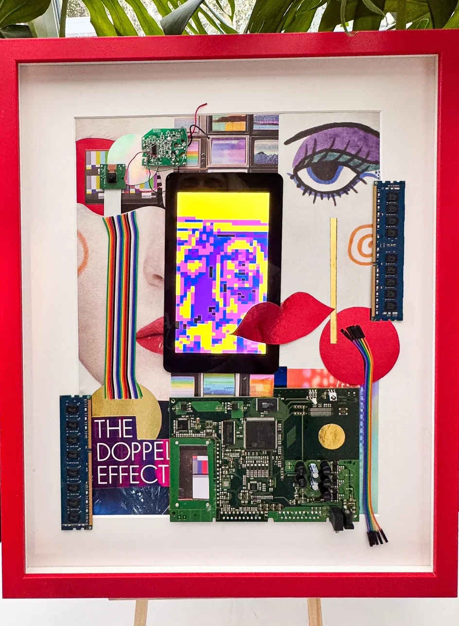 A framed assemblage on an easel: a screen showing a pixelated portrait among circuit boards, eyes and red lips, in a red box frame