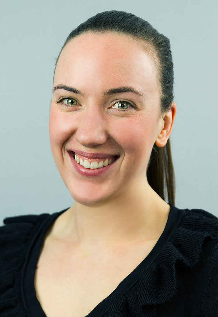 A woman with dark hair tied back, in a black top, smiling