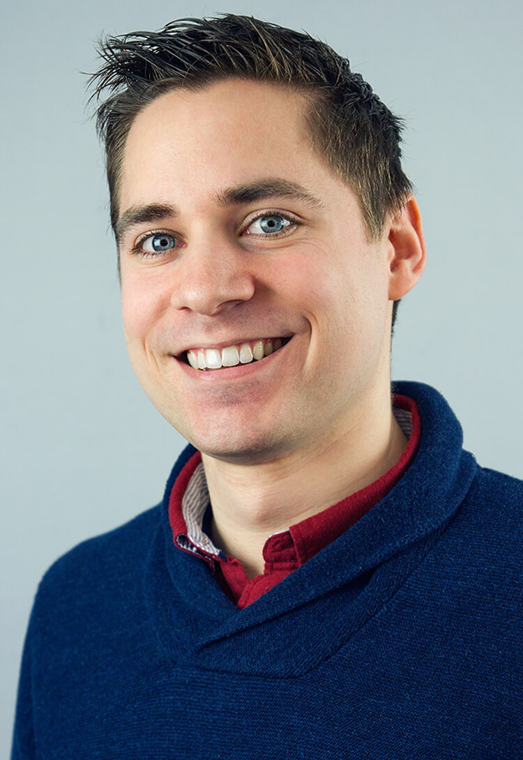 A man in a navy jumper over a dark red collar, smiling