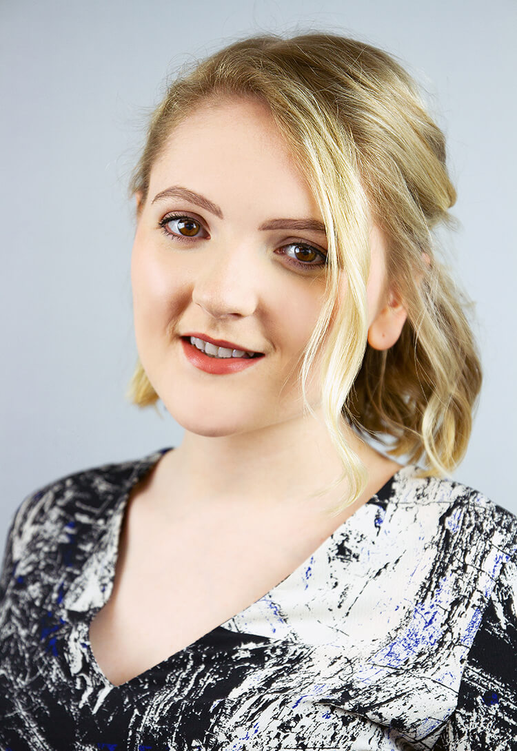 A woman with blonde hair swept to one side, in a patterned collared top