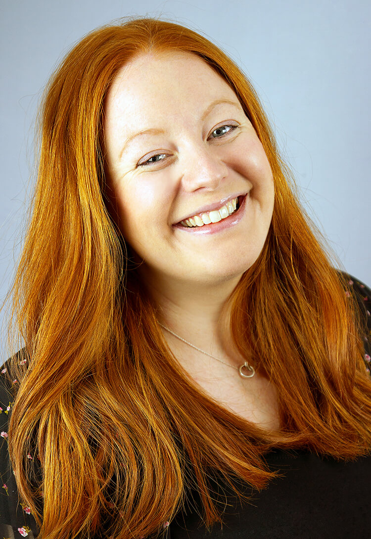 A woman with long red hair, laughing, against grey