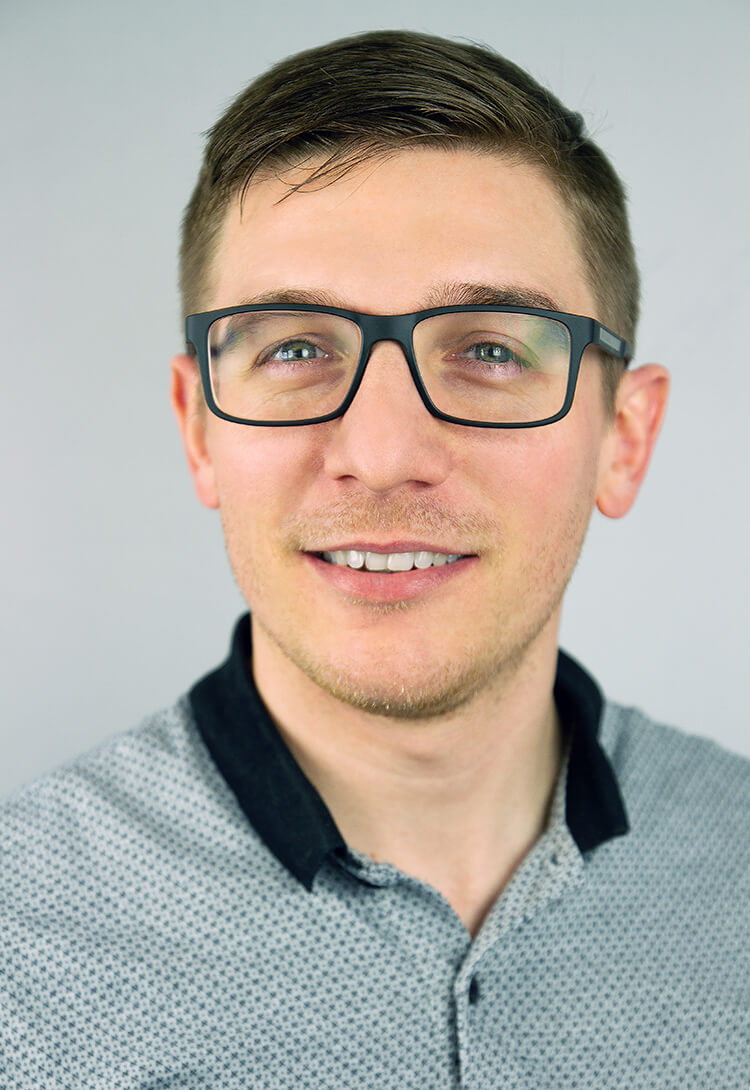 A man in dark-framed glasses and a grey polo shirt