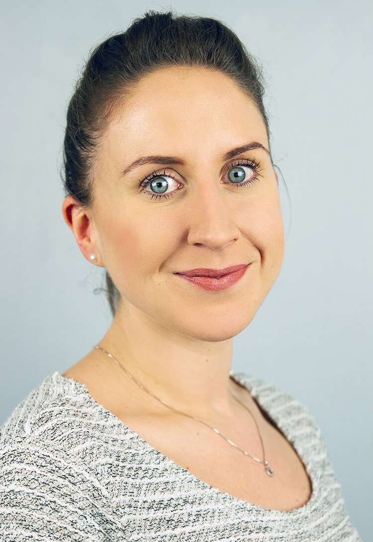 A woman with dark hair tied back, in a pale textured top