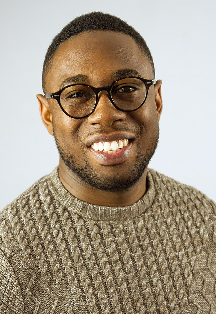 A man in round glasses and an oatmeal knitted jumper, smiling