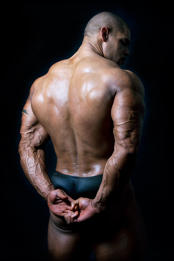 A bodybuilder photographed from behind against black