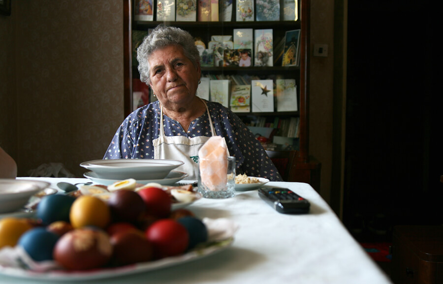 An older woman sitting at a table laid with painted Easter eggs