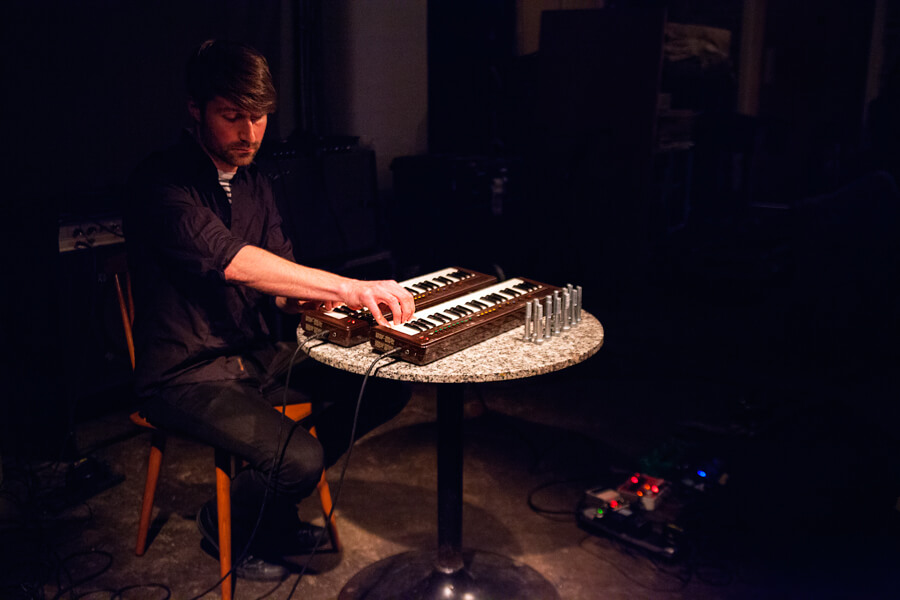 A musician playing a small electric keyboard on a dark stage