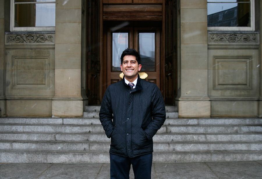A man in a dark coat on the steps of a stone civic building