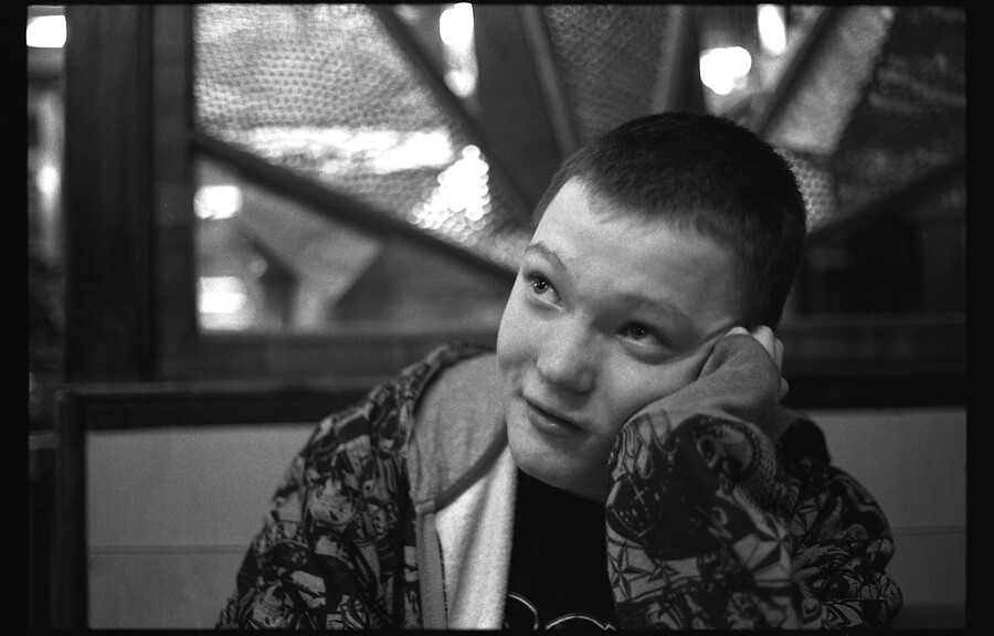 A young person resting a cheek on one hand, under the steel girders of a bridge