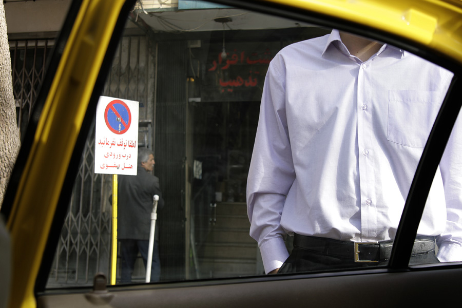 Seen from inside a yellow taxi, a man in a white shirt standing at a shopfront