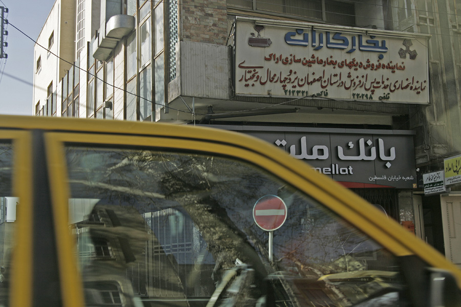 A yellow bus at the kerb below bank signage in Persian script