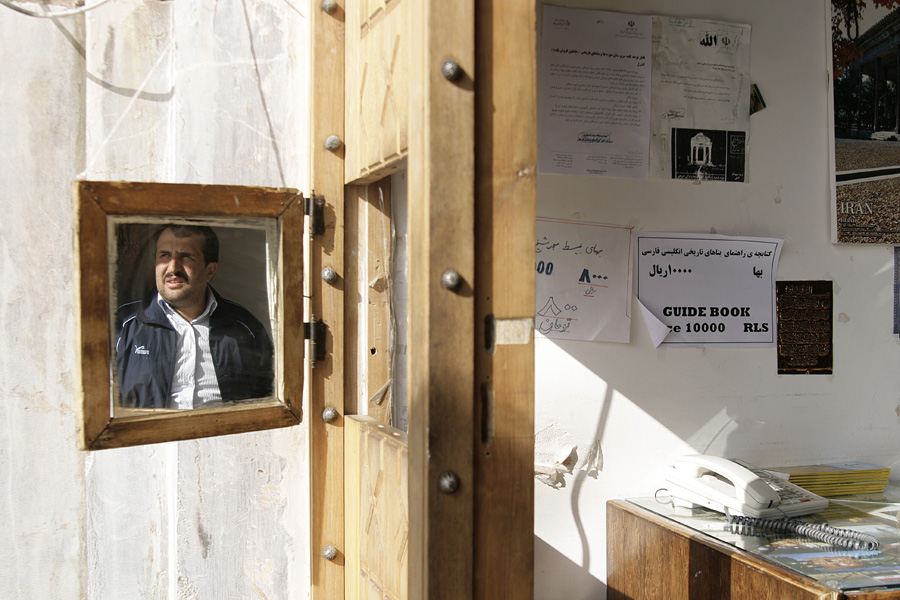 A framed photograph of a man on a wooden door, beside notices and a guide-book price list