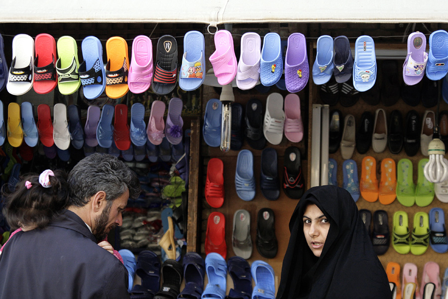 A stall hung with rows of coloured plastic sandals, a woman in a headscarf in front of it