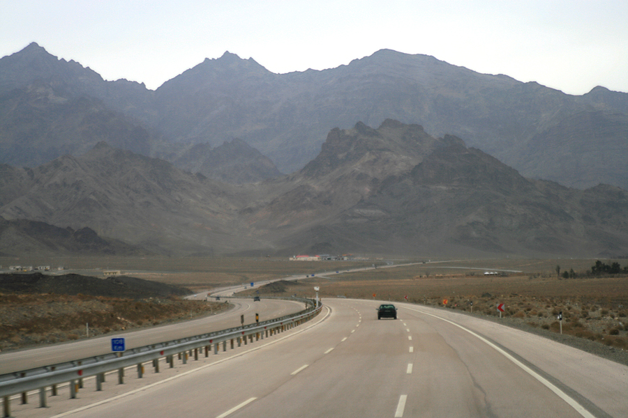 An empty highway curving through bare mountains