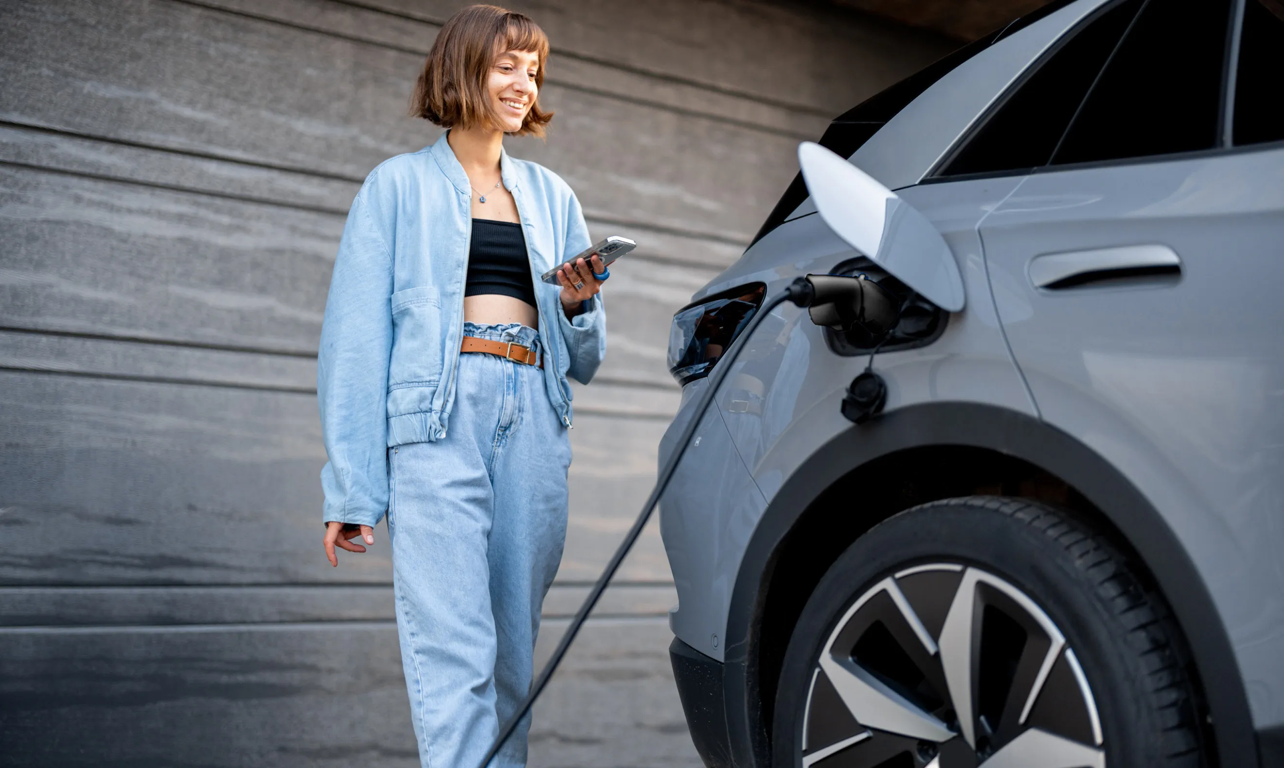 woman using mobile in front of a charging EV
